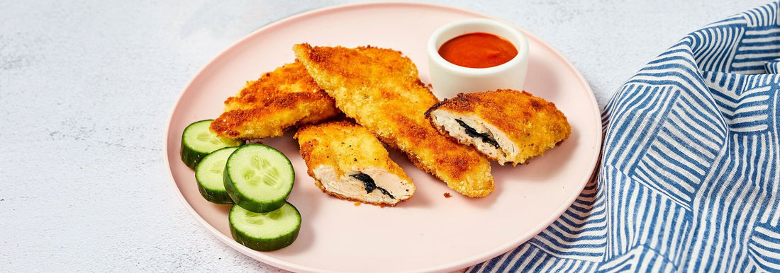 Chicken tenders on a pink plate with sliced cucumbers and dipping sauce.