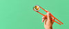 A hand holding red chopsticks grips a single piece of sushi with a green background.