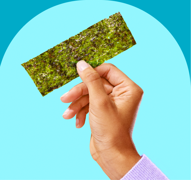 A hand holding a piece of green seaweed snack against a blue background.