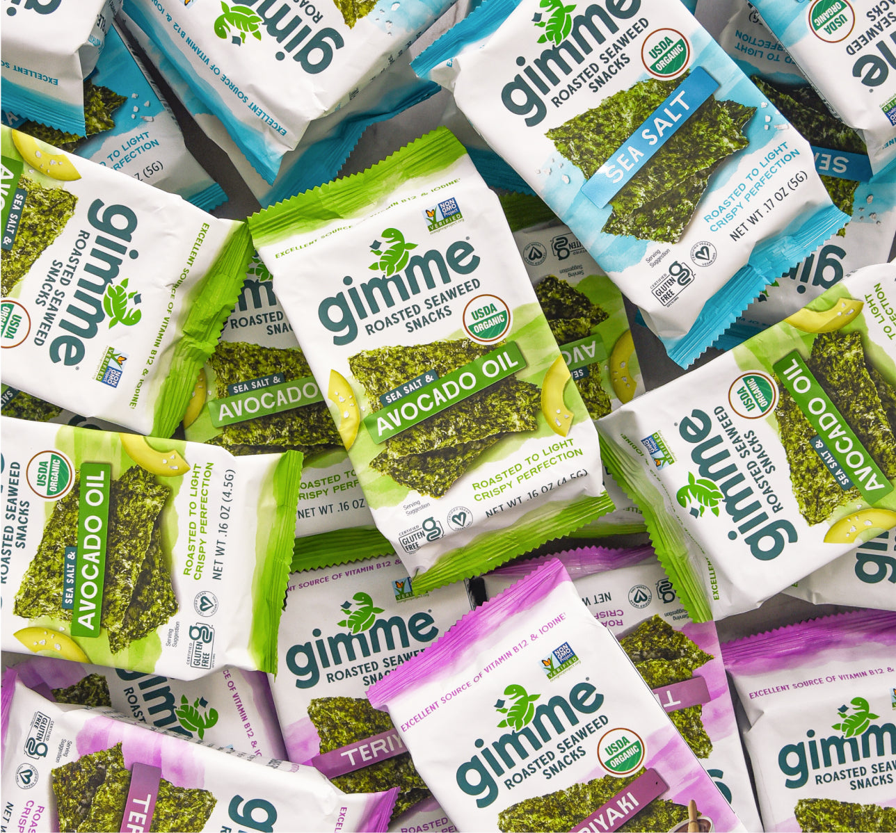 An assortment of Gimme roasted seaweed snack packs in various flavors including avocado oil, sea salt, and teriyaki, spread out in an overlapping pattern.