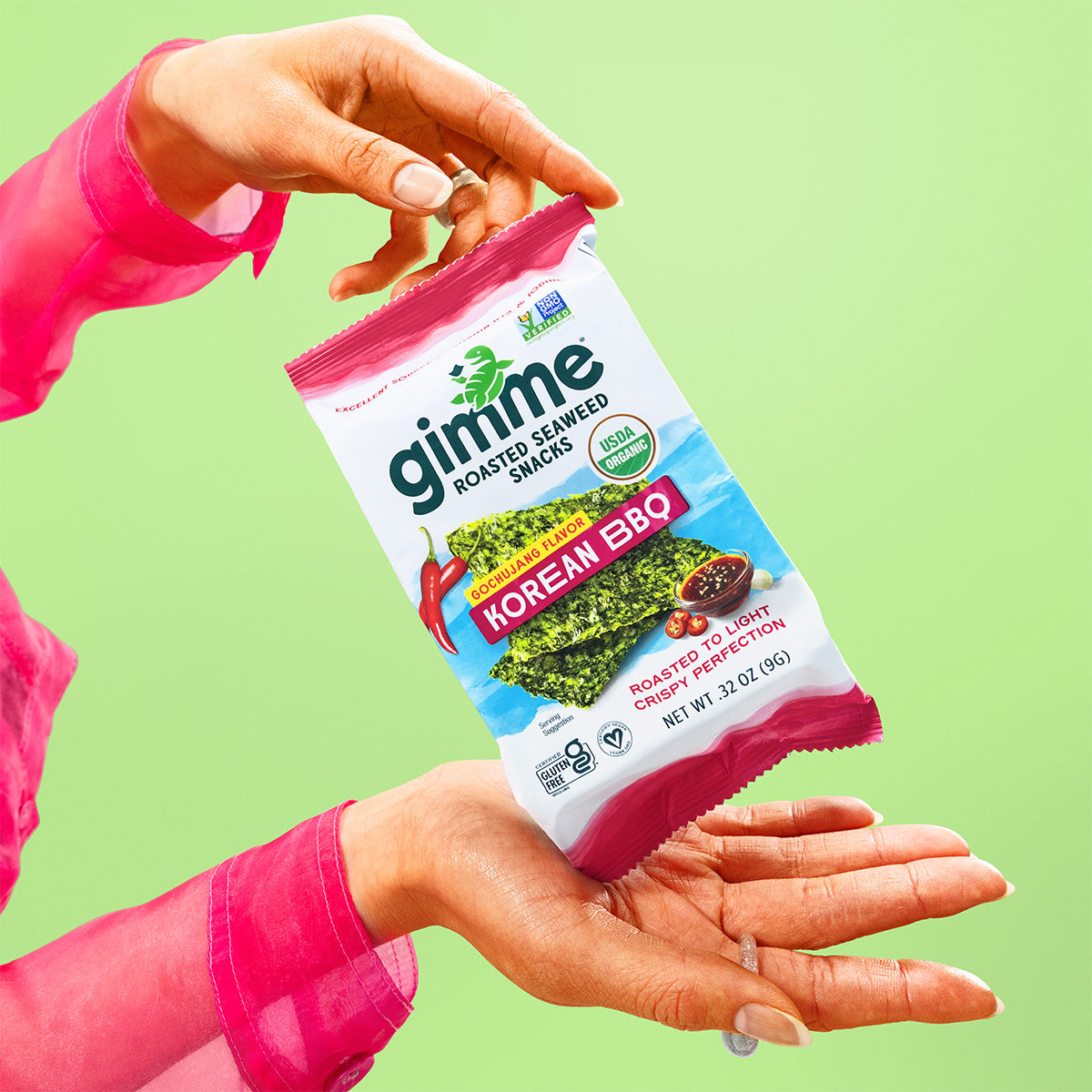 Hands holding a package of Gimme Roasted Seaweed Snacks Korean BBQ flavor against a green background